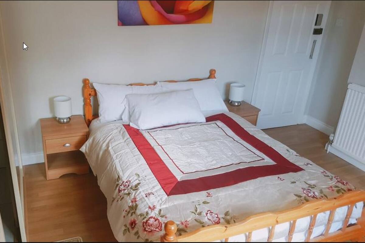 A neatly made bed with a floral bedspread and a red accent border. There are two bedside tables with lamps and a wooden headboard.