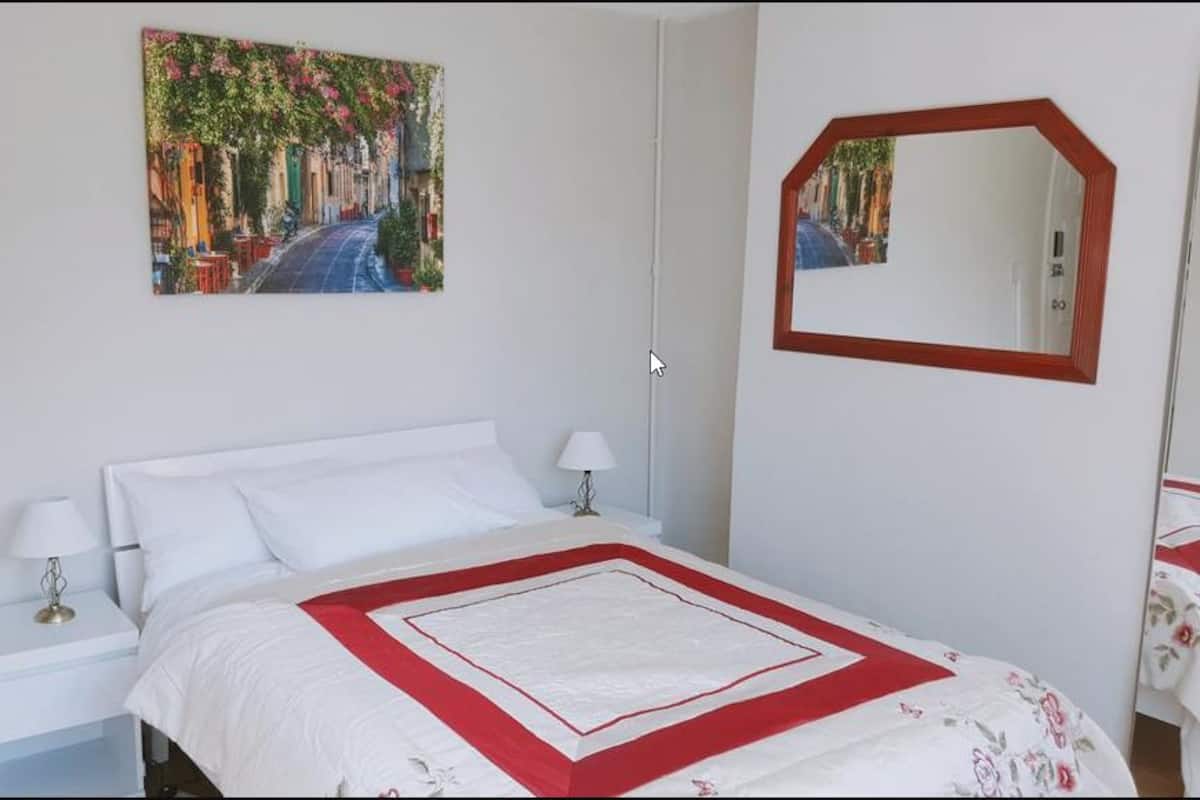 A neatly arranged bedroom with a bed, bedside tables, a mirror, and a painting on the wall.
