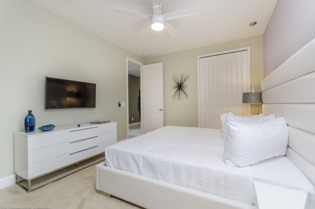 Ein Schlafzimmer mit Bett, Fernseher, Kommode und Deckenventilator.