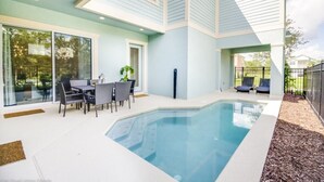 Ein modernes Haus mit Swimmingpool, einer Terrasse und Gartenmöbeln sowie einer großen Glasschiebetür.