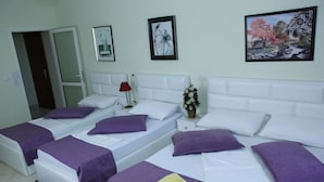 A hotel room with two beds, each with white bedding and purple pillows. There are framed pictures on the wall, a vase with flowers, and a red lamp on the nightstand. - Hotel Bicaj (Shkodër)