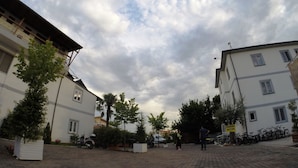 A paved courtyard with buildings, trees, and parked vehicles. - Hotel Bicaj (Shkodër)