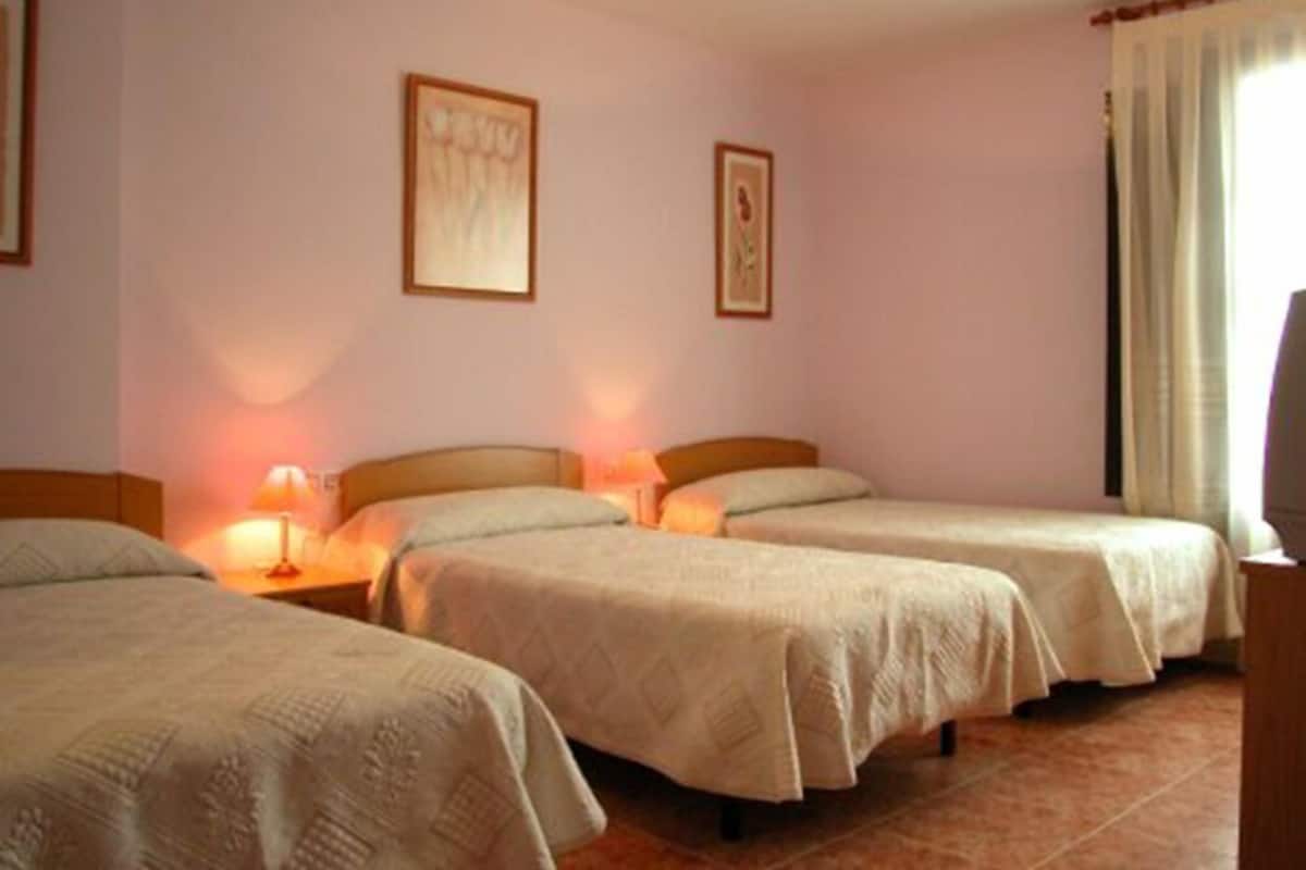 A hotel room with two single beds, a nightstand with a lamp, and a television.