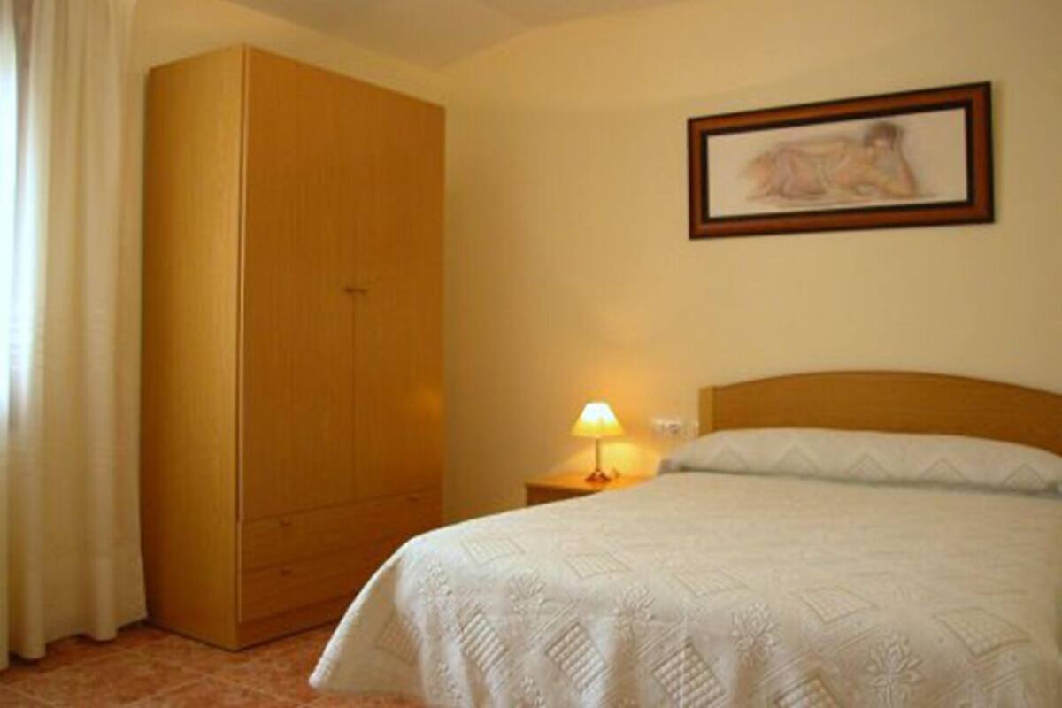 A hotel room with a bed, a nightstand with a lamp, a wardrobe, and a framed picture on the wall.