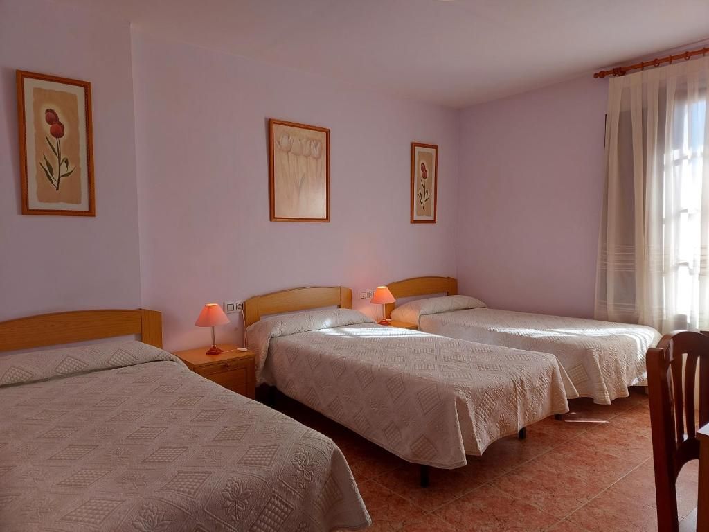 Quarto de hotel com três camas de solteiro, cabeceira de madeira, mesa de cabeceira com abajur e uma cadeira.