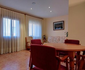 A dining area with a round table and chairs, a sofa, and a window with curtains. - Hostal Castilla (Serón de Nágima)