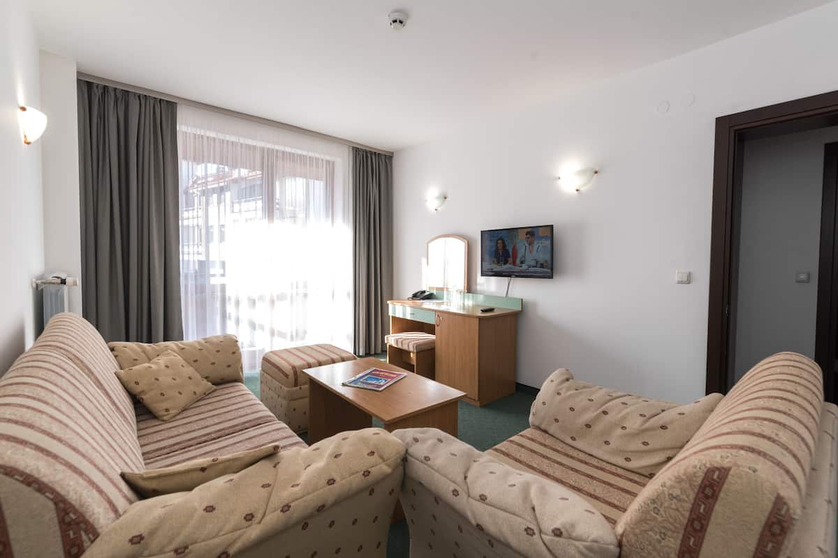 A hotel room with a sofa set, a small desk, a television, and a large window with curtains.