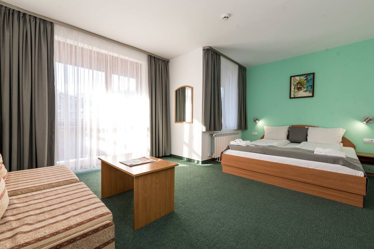 A hotel room with a bed, a desk, a chair, and a large window with curtains.