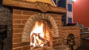 A brick fireplace with a fire burning inside, a wooden mantel above it, and a brick wall in the background. - Iceberg (Bansko)