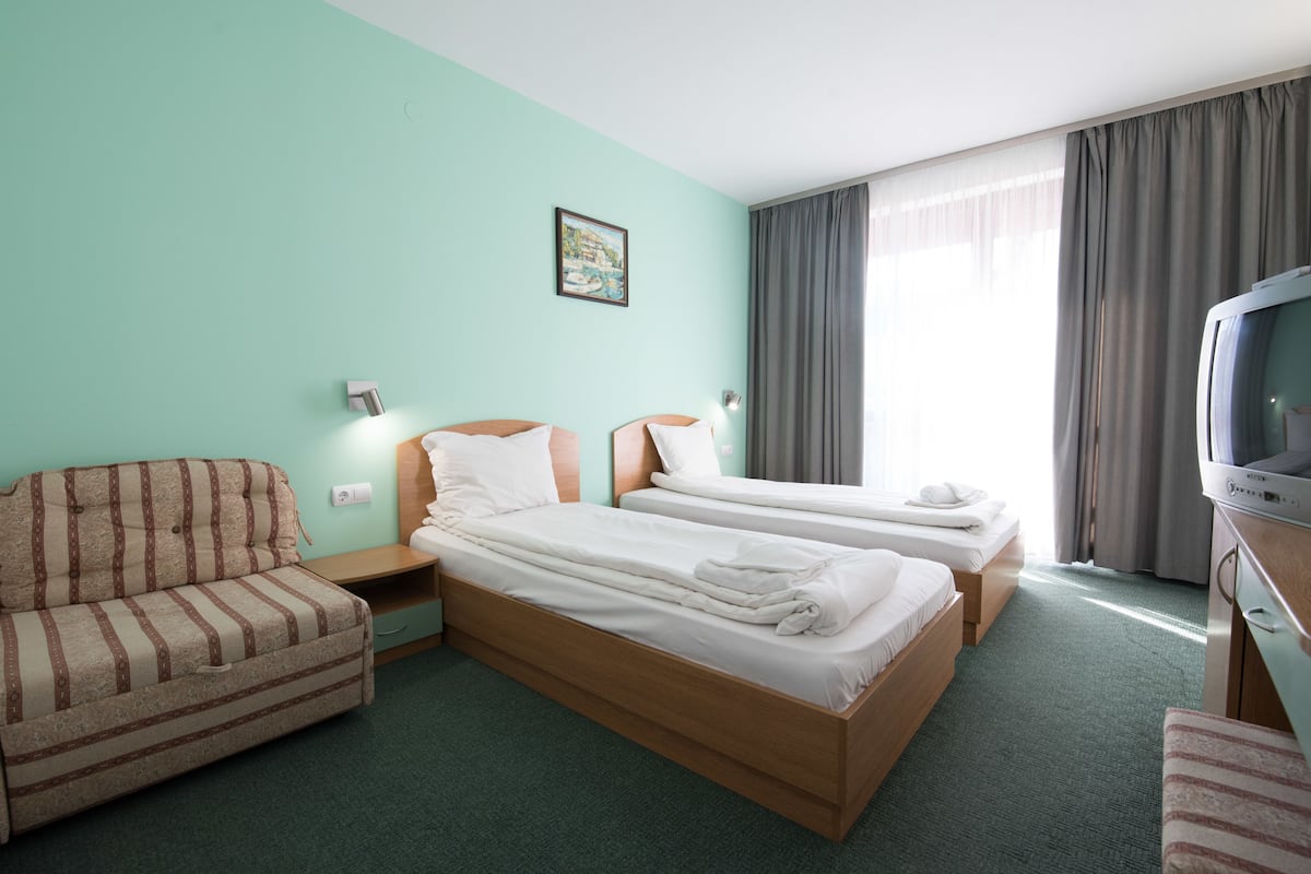 A hotel room with two single beds, a sofa, a television, and a painting on the wall.