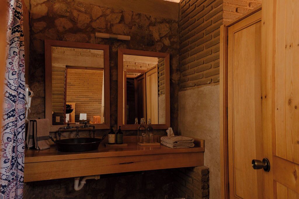 Un baño rústico con un tocador de madera, dos espejos, un lavabo negro y una puerta de madera.