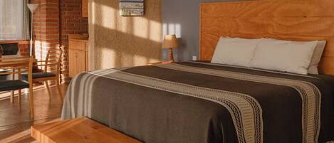 Un dormitorio con cama de madera, un banco, un ventilador de techo y una pared de ladrillo.