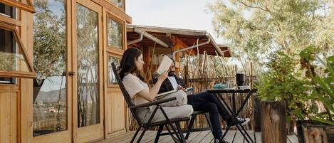 Una terraza de madera con dos personas sentadas en una mesa, leyendo.