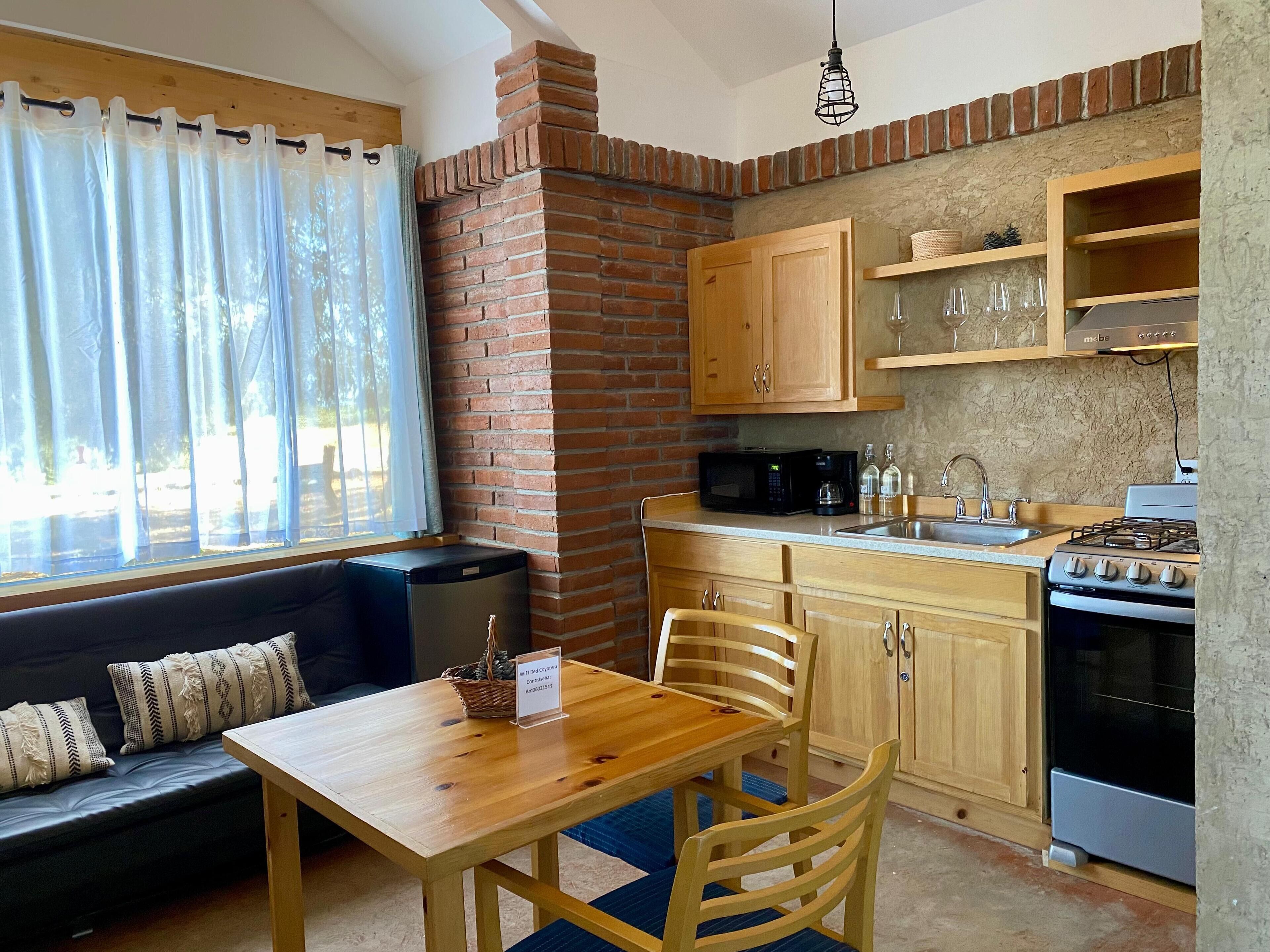 Una cocina compacta con pared de ladrillo, armarios de madera, microondas, estufa y comedor con mesa y sillas.