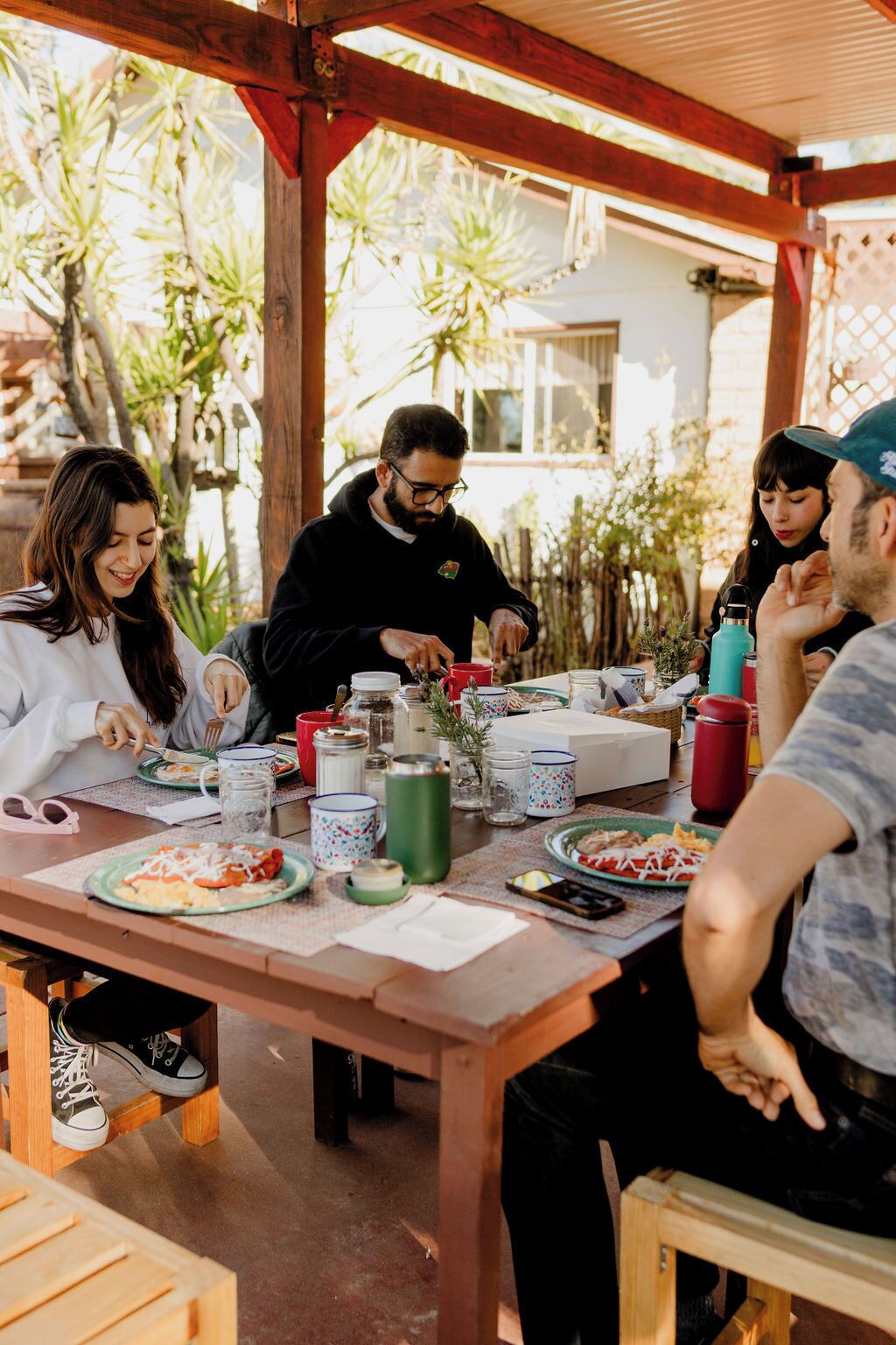 A group of people dining at an outdoor wooden table with various dishes and drinks.