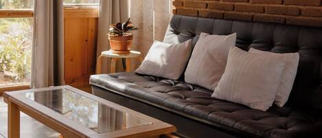 A cozy living room with a dark leather sofa, a glass coffee table, and a brick accent wall with framed pictures.