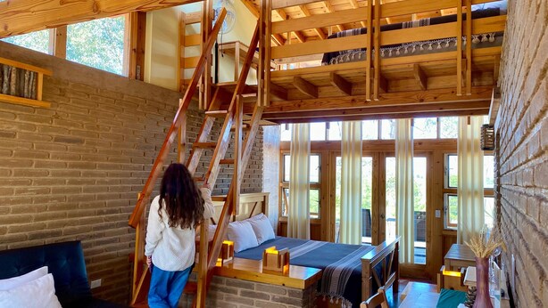 Een rustiek houten interieur met een hoogslaper, een trap en een bakstenen muur.