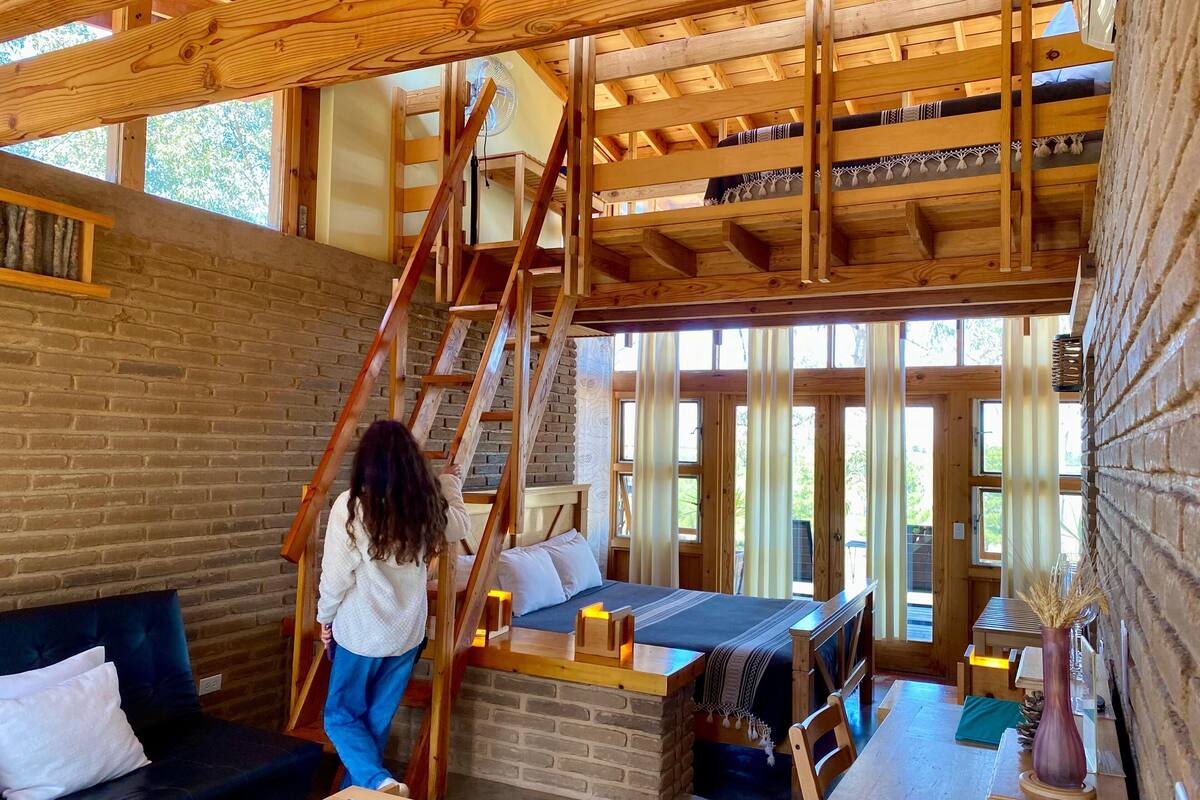 A rustic wooden interior with a loft bed, a staircase, and a brick wall.