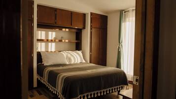 Une chambre à coucher avec un lit, des armoires en bois et une fenêtre avec des rideaux.