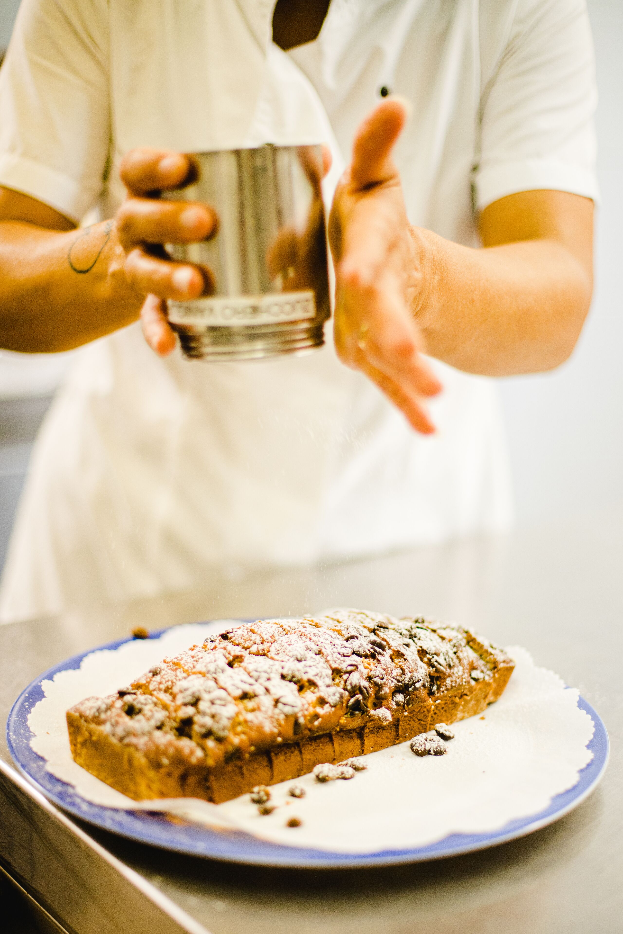 A person holding a glass of water over a plate with a loaf of bread.