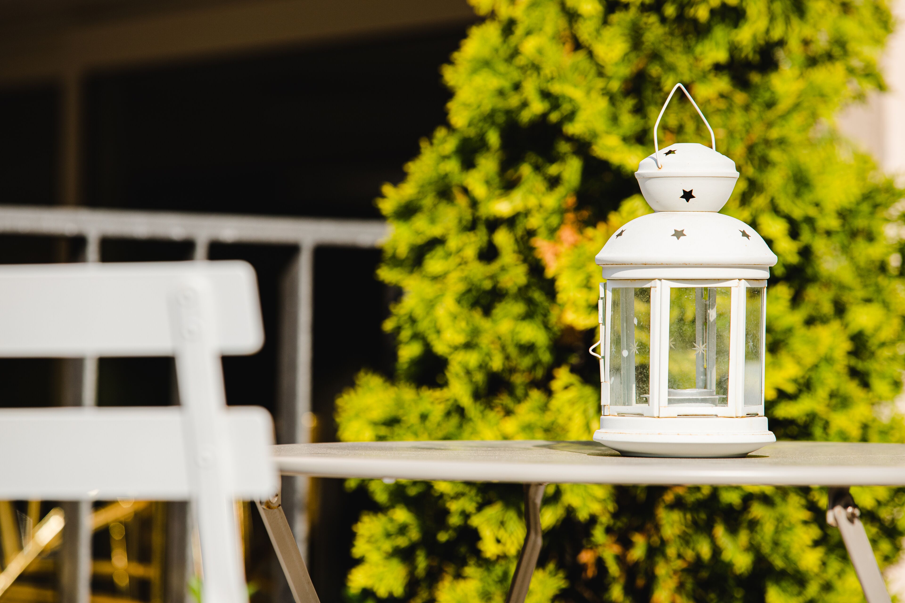 A white lantern on a table with a green tree in the background.