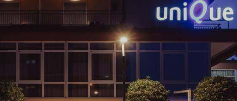 Un edificio con un letrero que dice "uniQue", varios balcones y una entrada iluminada con asientos al aire libre.