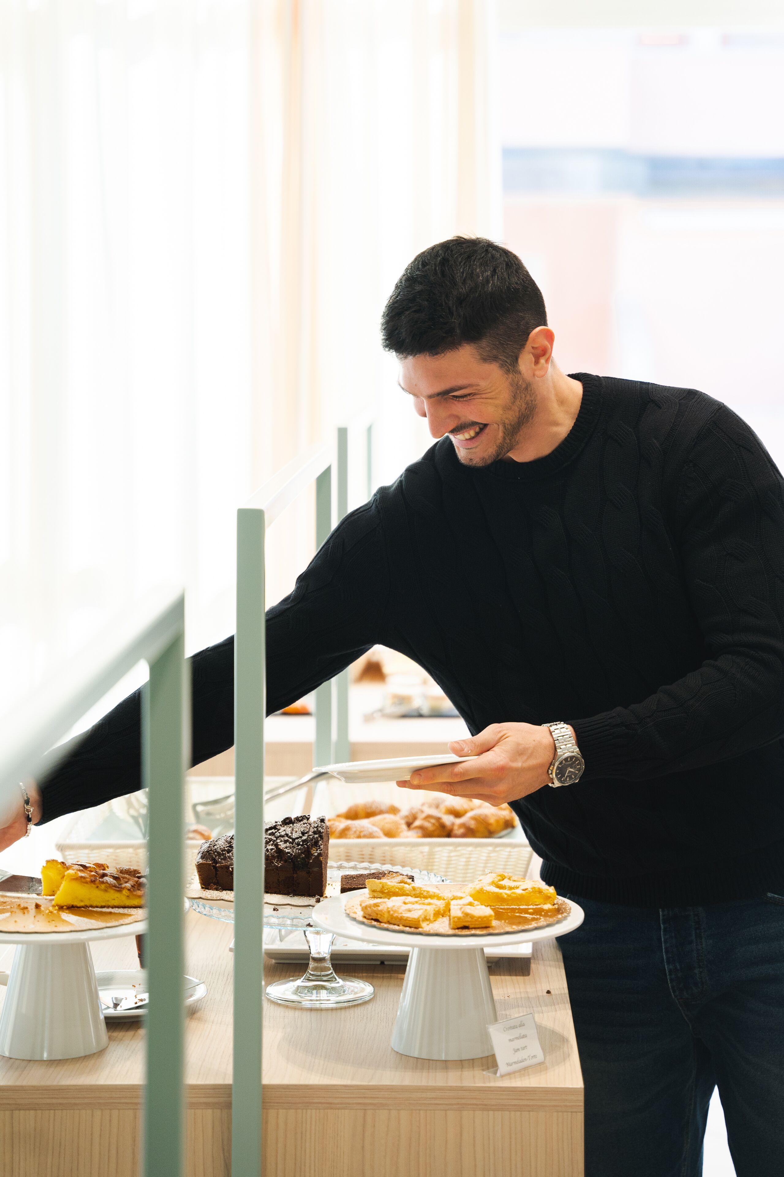 A person serving food from a buffet table with various desserts and pastries.
