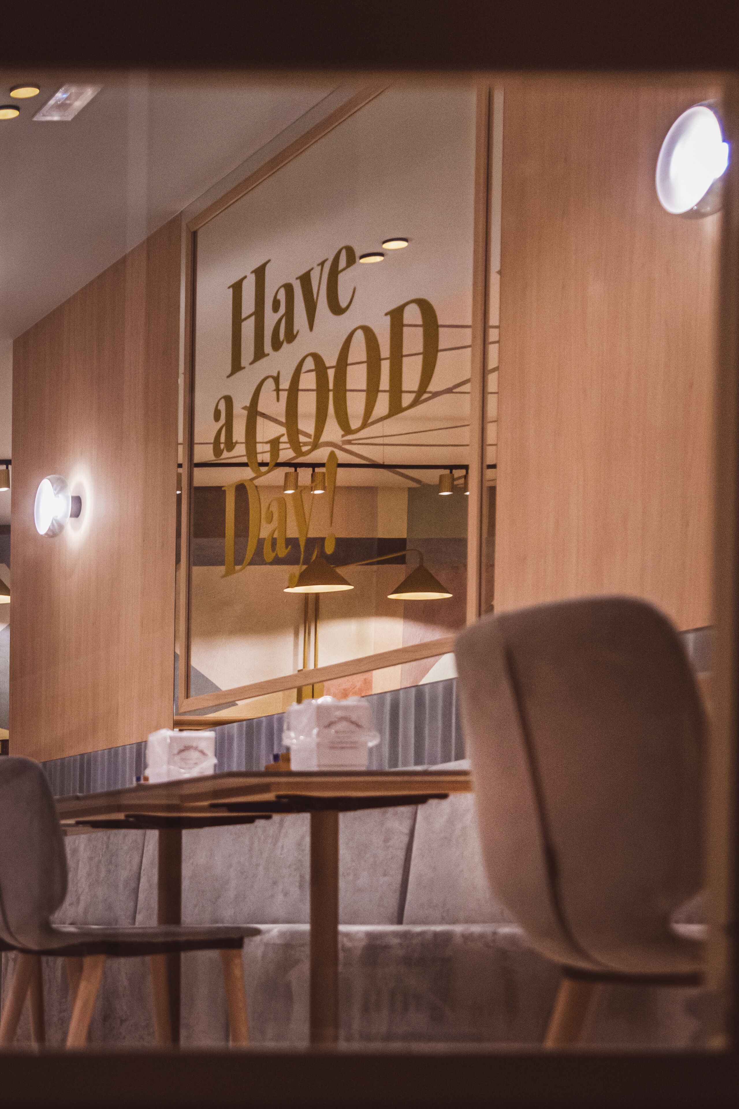 A dining area with a table and chairs, a wall with a 'Have a good day!' sign, and a mirror reflecting the interior.