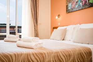 A hotel room with a bed, pillows, a headboard, a window with curtains, and a wall-mounted light fixture. - Unique Hotel (Cesenatico)