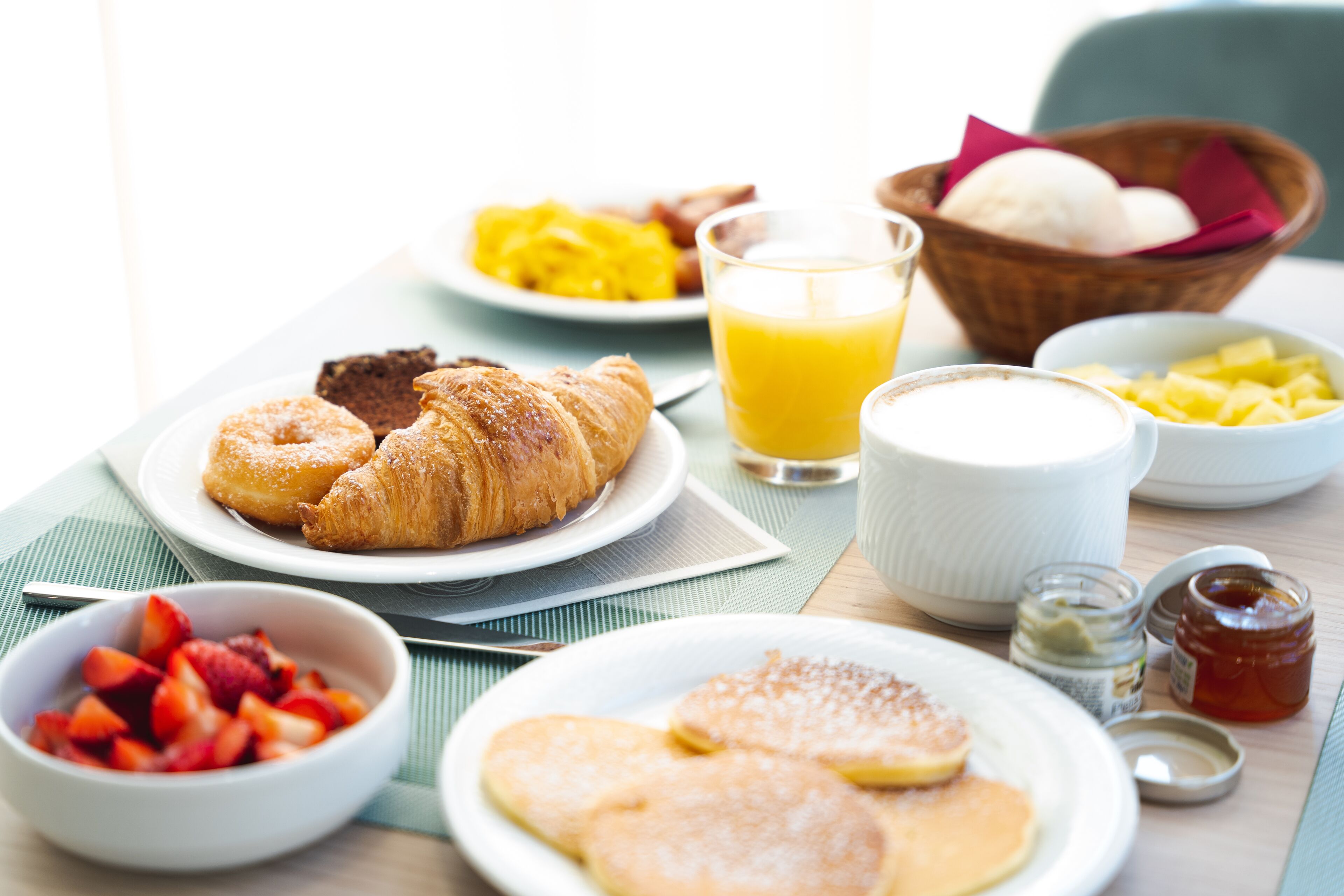 Una mesa de desayuno con cruasanes, panqueques, fruta y un vaso de zumo de naranja.