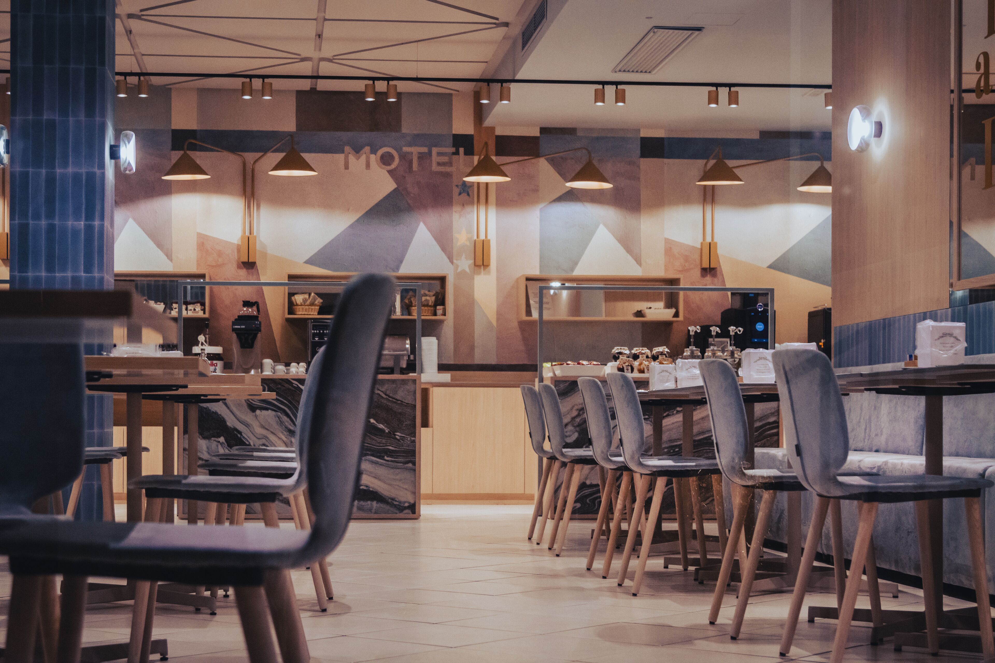 A modern motel interior with a central dining area, multiple tables, and chairs.