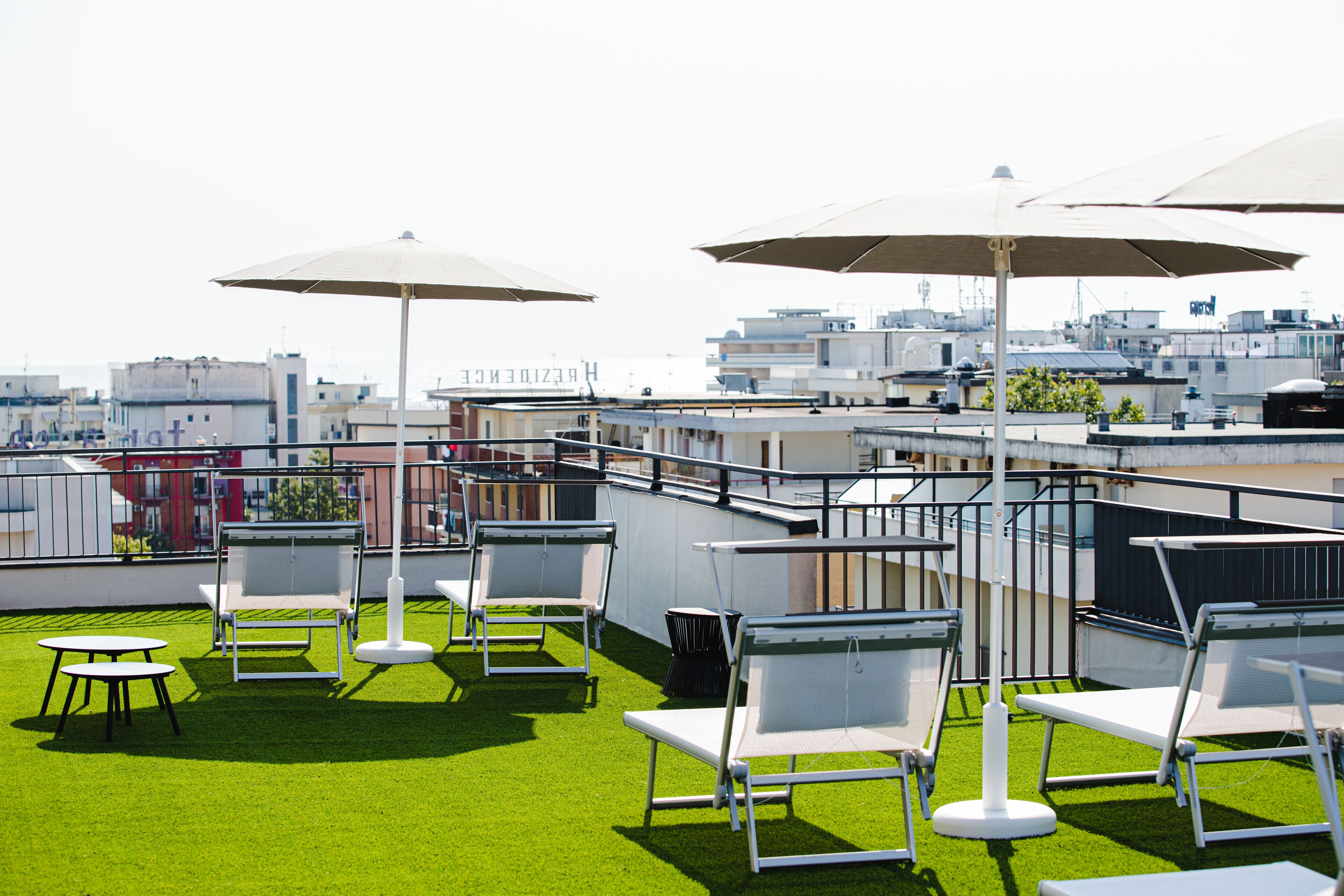 A rooftop terrace with white chairs and tables, large umbrellas, and a view of the cityscape.