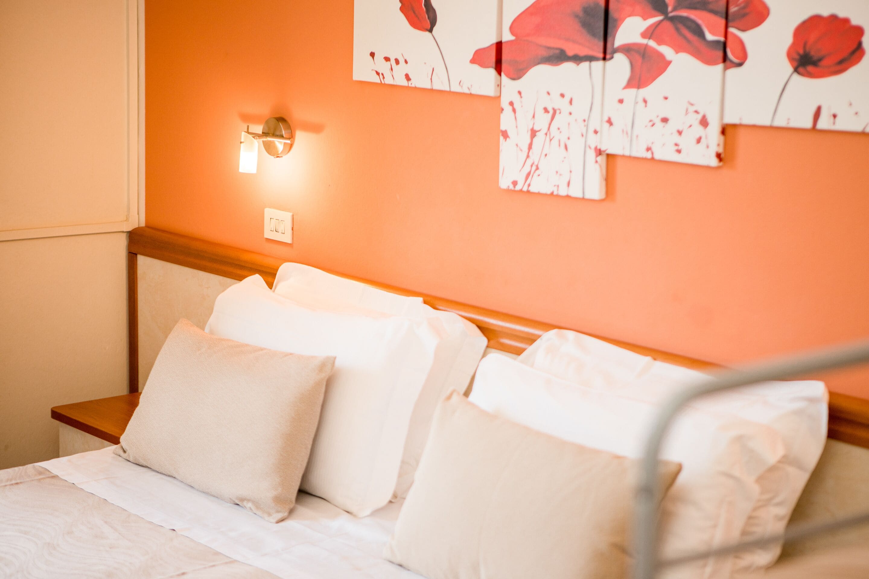 Una cama bien hecha con sábanas y almohadas blancas, un cabecero de madera y una lámpara de pared.