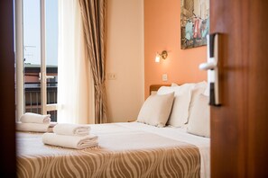 A hotel room with a bed, pillows, a window with curtains, a wall-mounted light, and a painting. - Unique Hotel (Cesenatico)