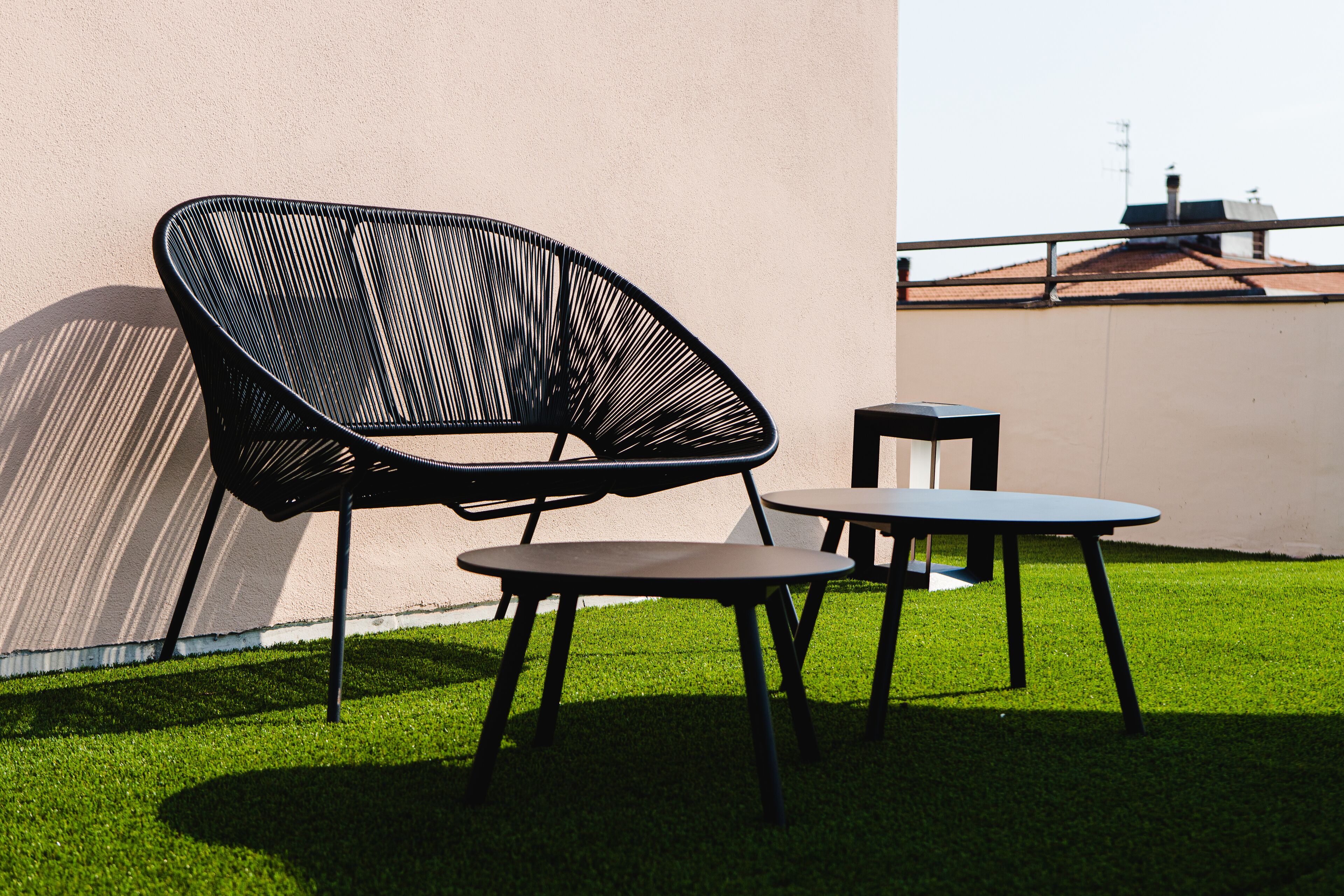 Un patio con una silla negra y dos mesitas, una pared y un edificio al fondo.