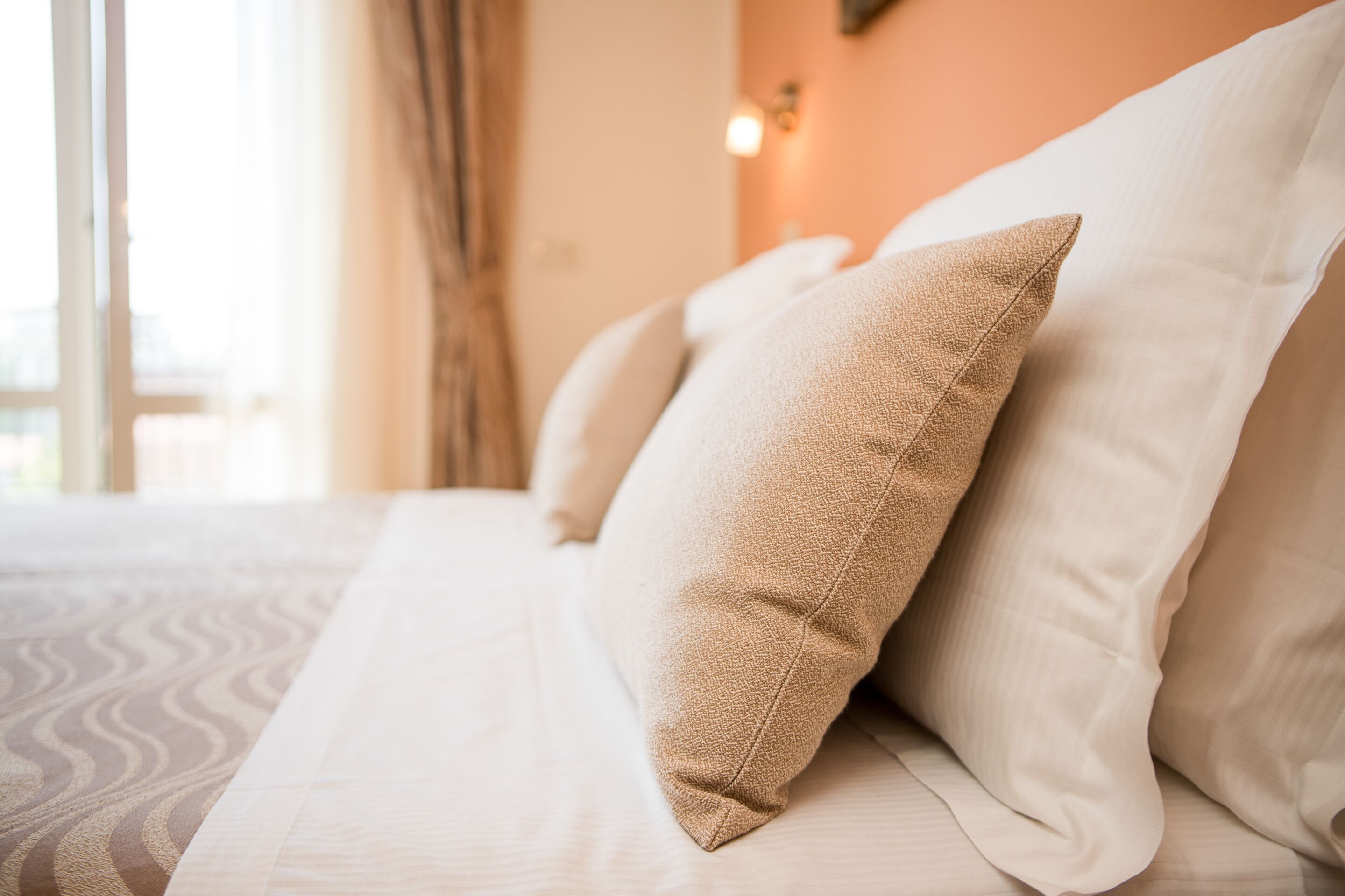 Una cama bien hecha con sábanas blancas y almohadas color beige.
