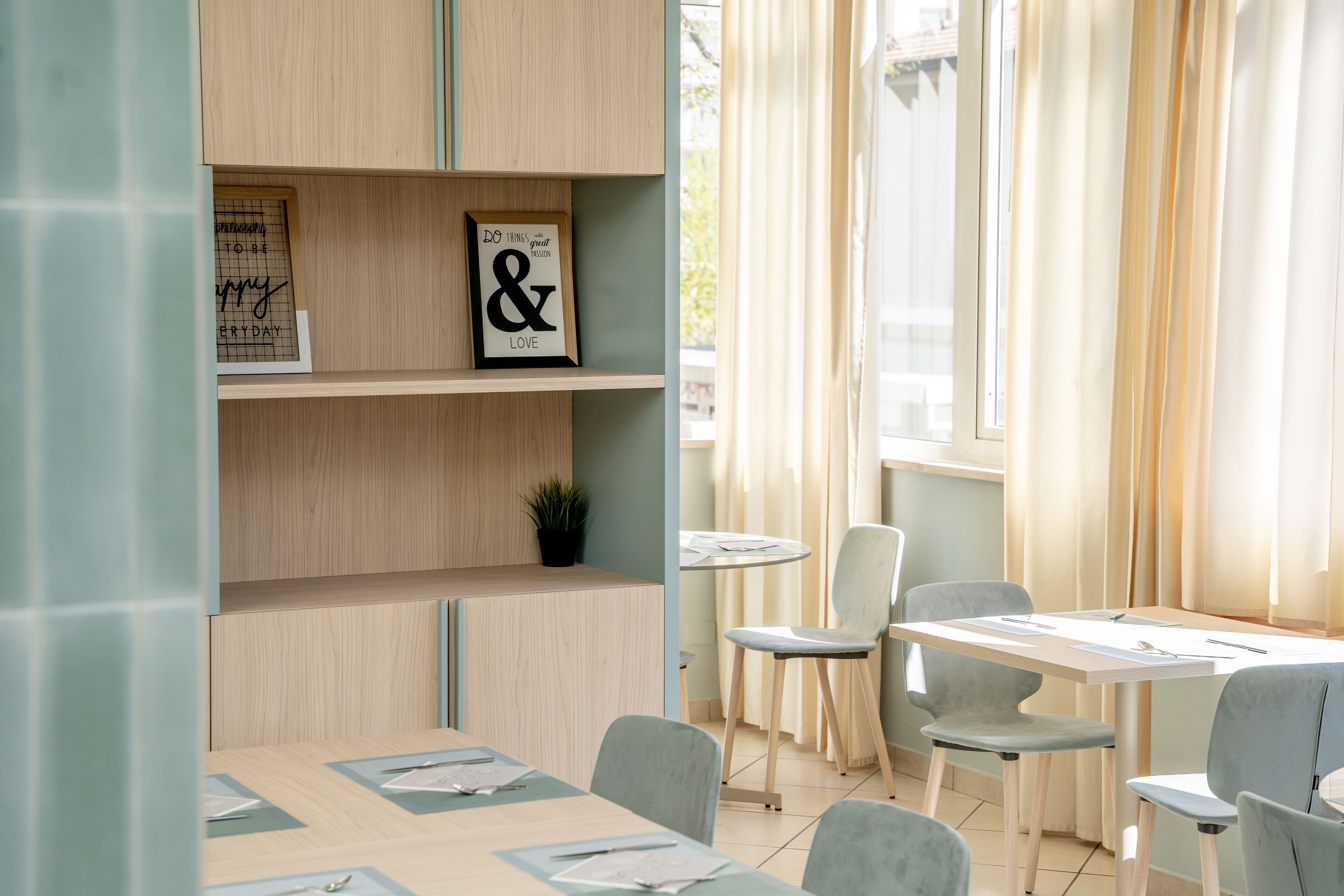 A modern dining area with a wooden table and chairs, a small potted plant, and a window with curtains.