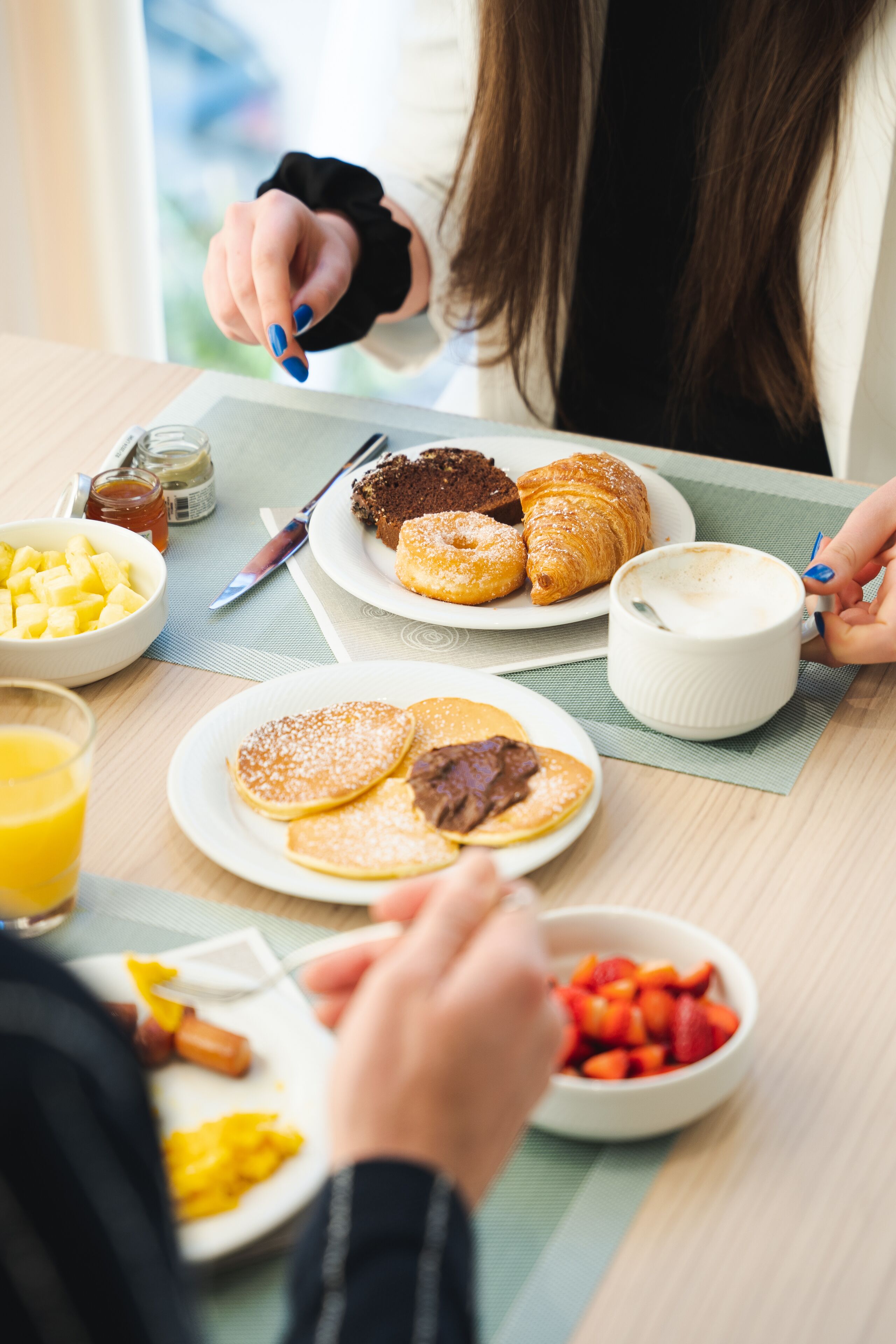 A breakfast table with plates of pancakes, croissants, and a hot beverage.