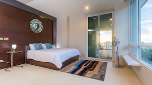 Un dormitorio moderno con una cama grande, una mesita de noche con lámpara, un espejo decorativo, una puerta corrediza de vidrio a un balcón y vistas de la ciudad.