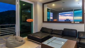 Una sala de estar moderna con un sofá grande de cuero negro, una mesa de centro de vidrio y un espejo grande que refleja una vista del atardecer.
