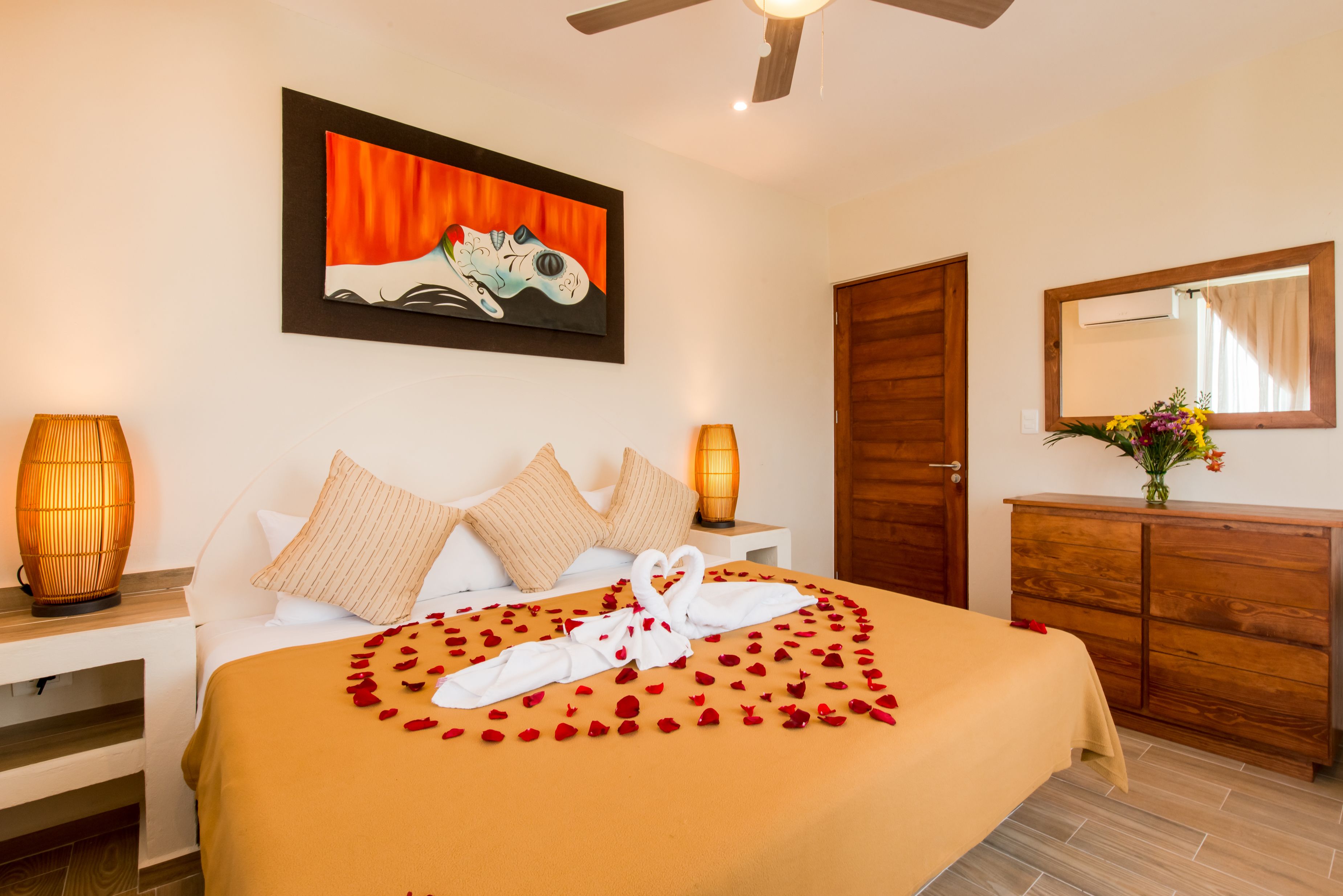 A hotel room with a bed, a painting, a wooden wardrobe, and a nightstand with a lamp.