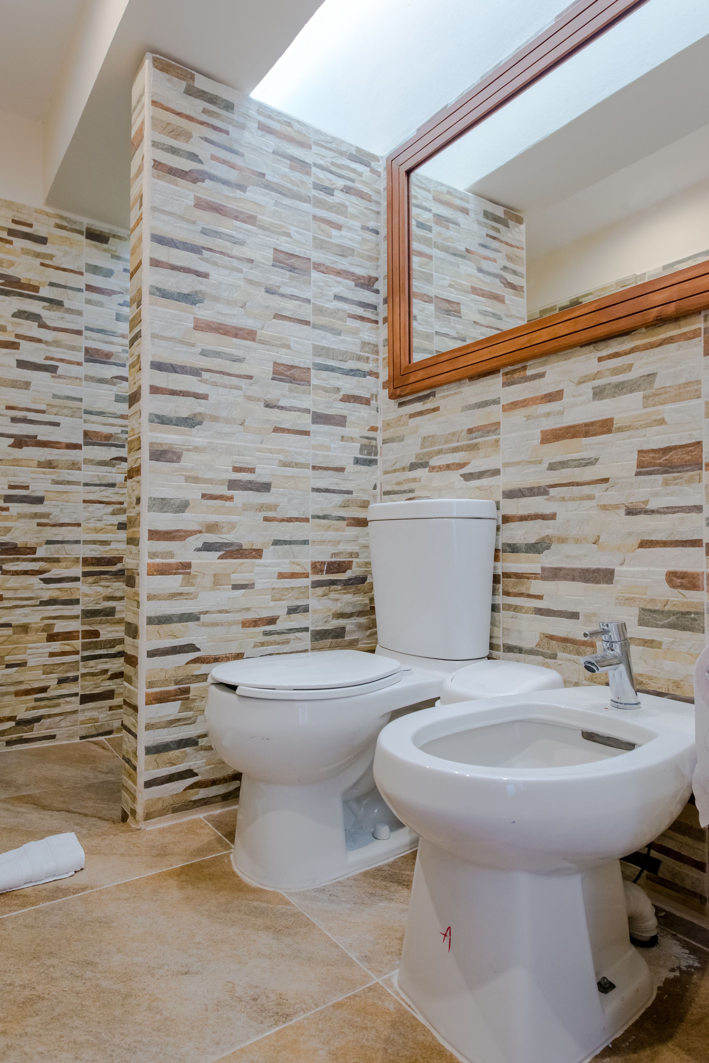 A bathroom with a stone-patterned wall, a toilet, a bidet, and a mirror.