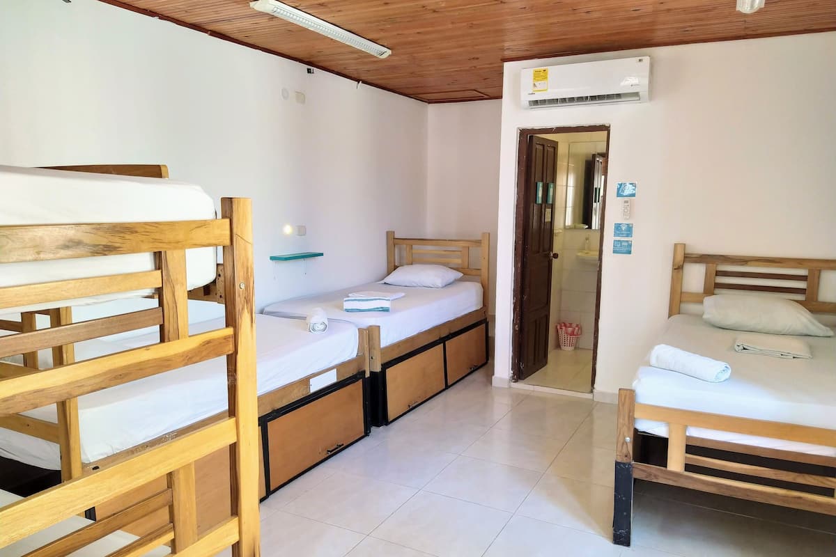 A room with three wooden bunk beds, a small shelf, an air conditioning unit, and a door leading to a bathroom.