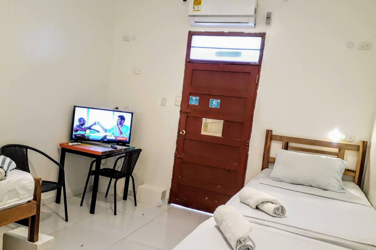 A hotel room with a bed, a TV on a desk, a chair, and a door with a window.