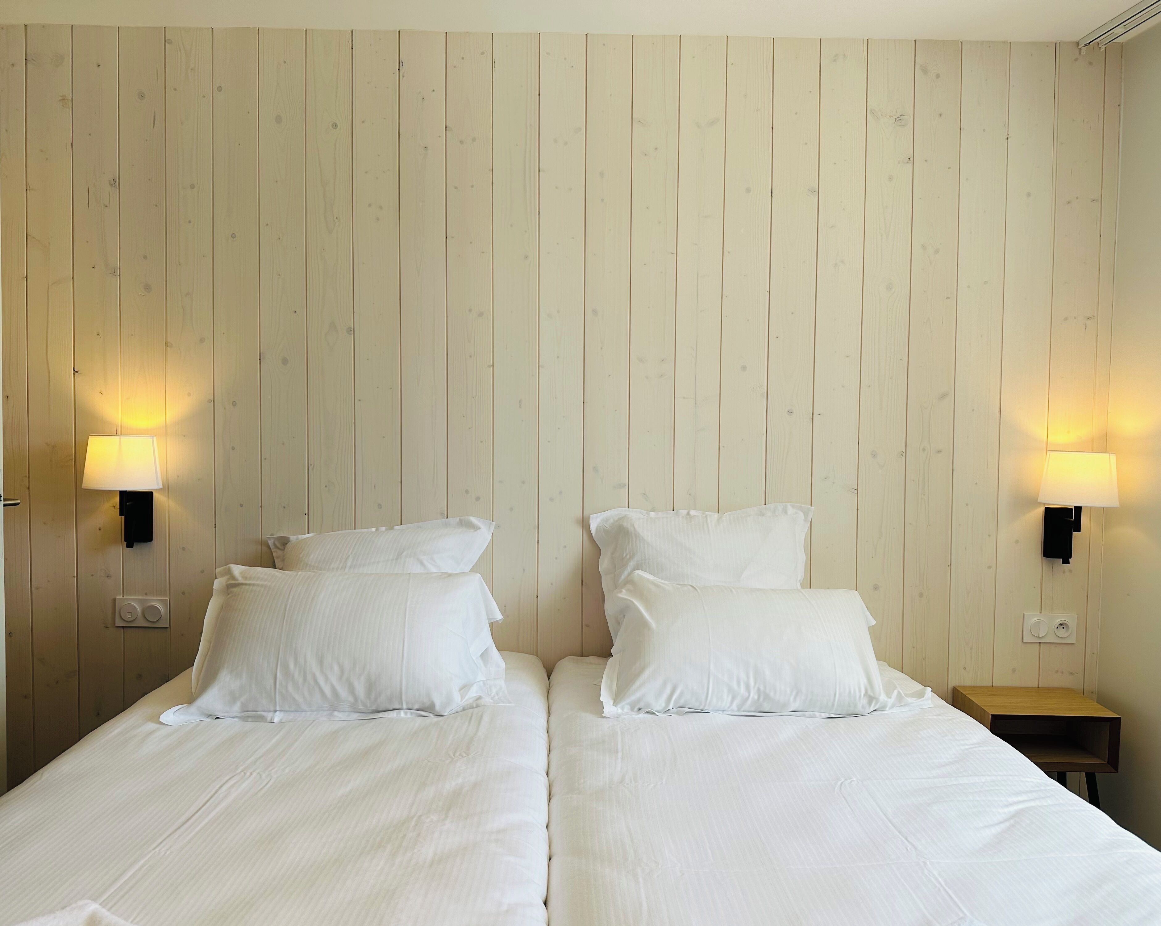 A double bed with white bedding and two wall-mounted lamps on either side.