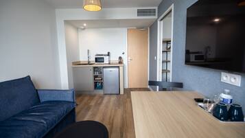 Un espacio habitable compacto con un sofá, una mesa de comedor y una kitchenette al fondo.