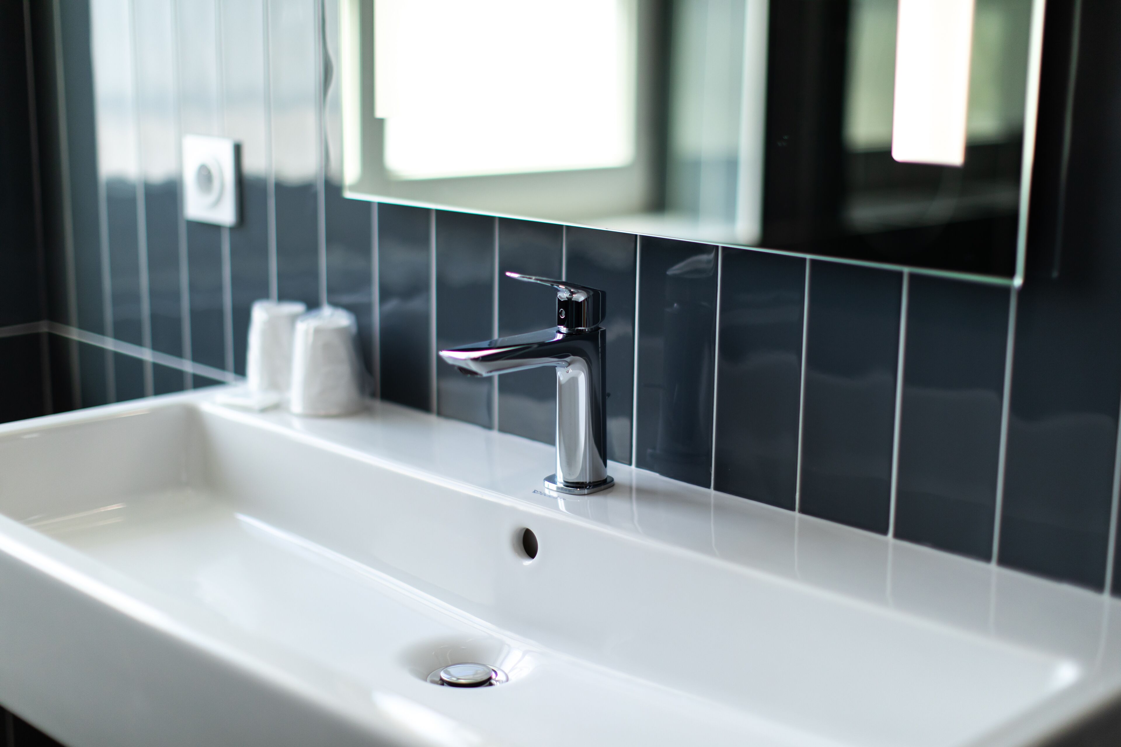 A modern bathroom with a white sink, chrome faucet, and black tiled walls.