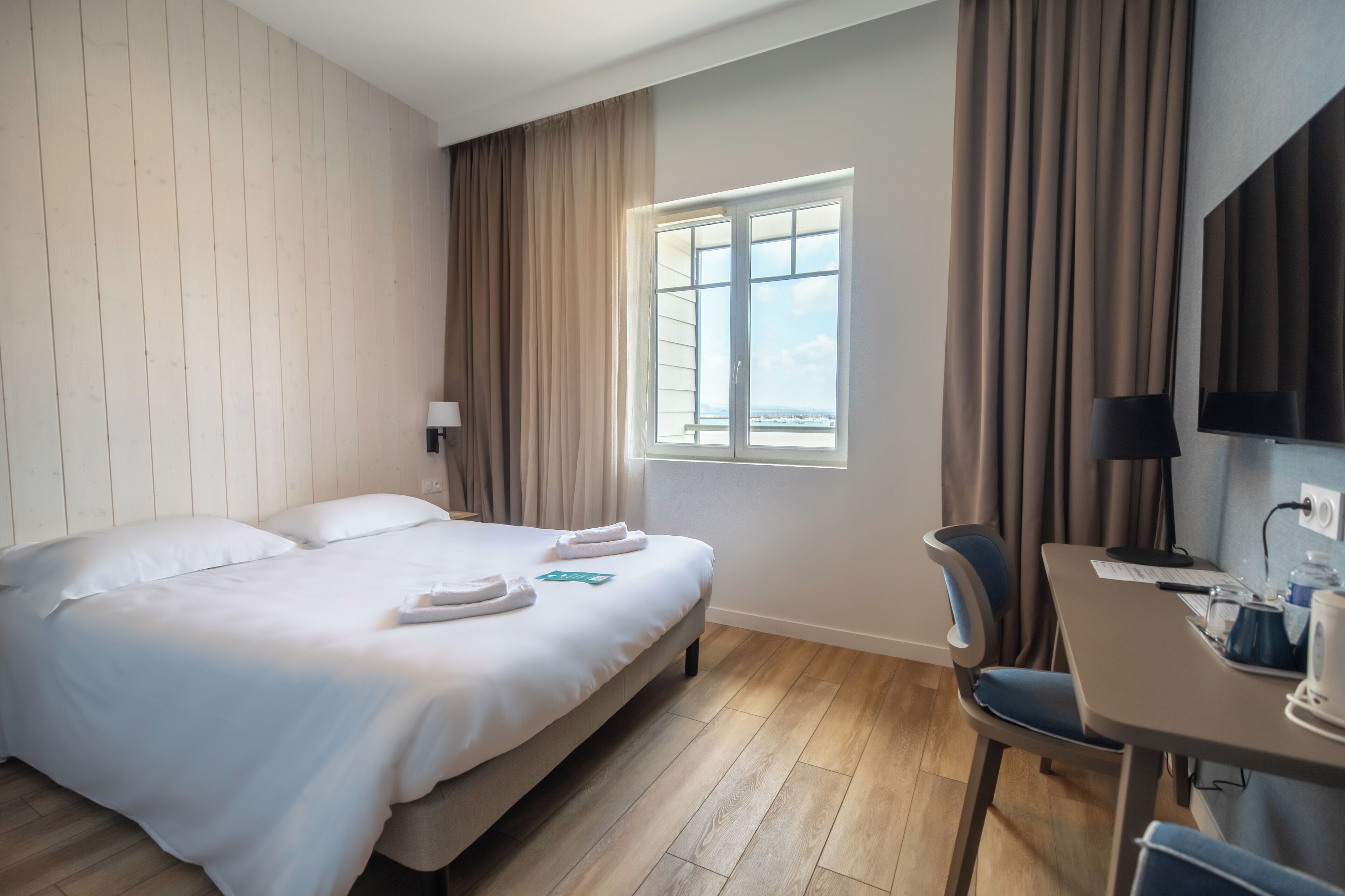 Ein Hotelzimmer mit Bett, Schreibtisch, Stuhl, Fernseher und einem Fenster mit Vorhängen.
