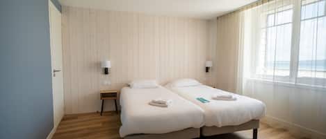Una habitación con dos camas, una mesita y una ventana con cortinas.
