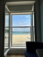 Quarto com uma grande janela com vista para a praia, piso de madeira e uma cadeira azul.